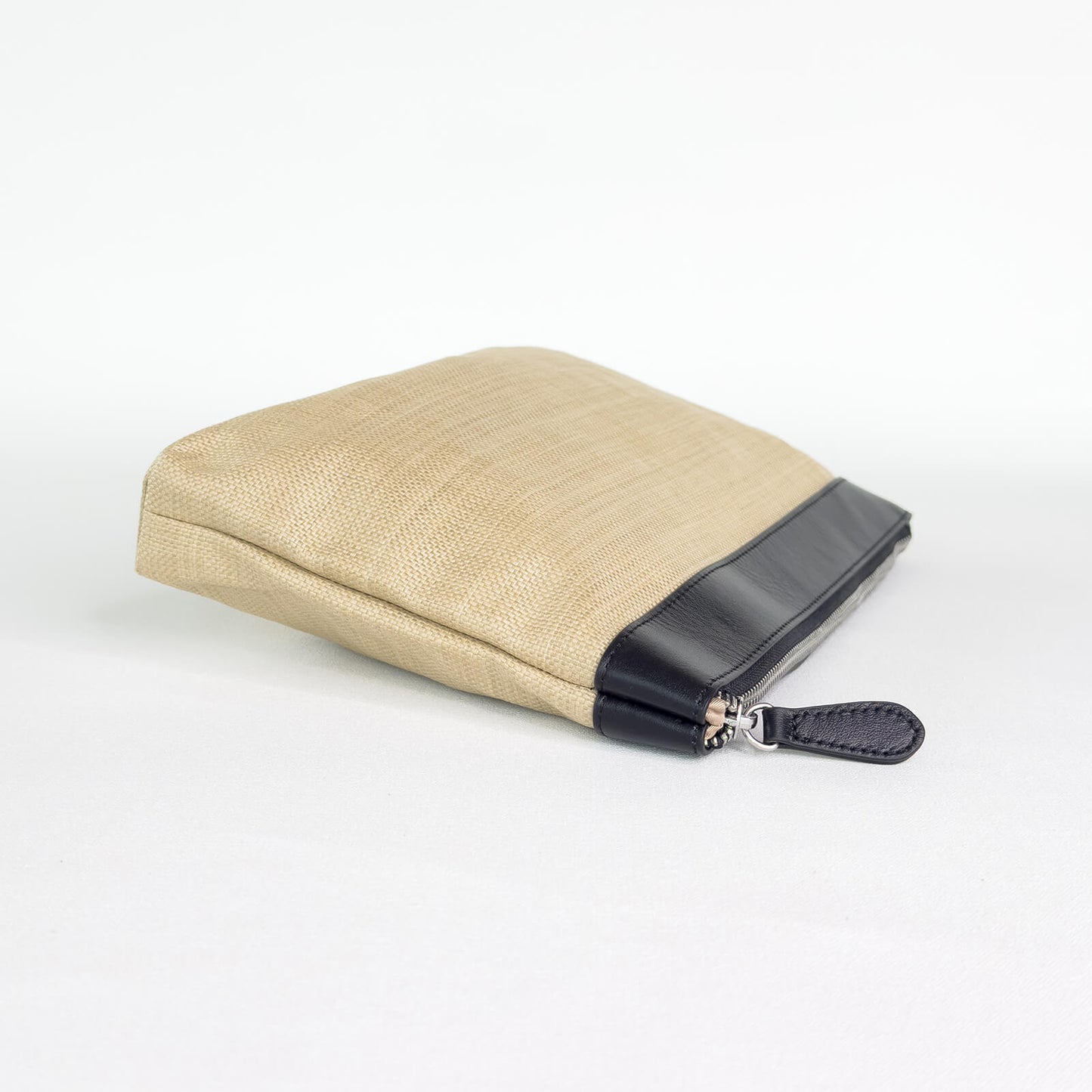 Beige pouch with black leather trim and black zipper on a white background