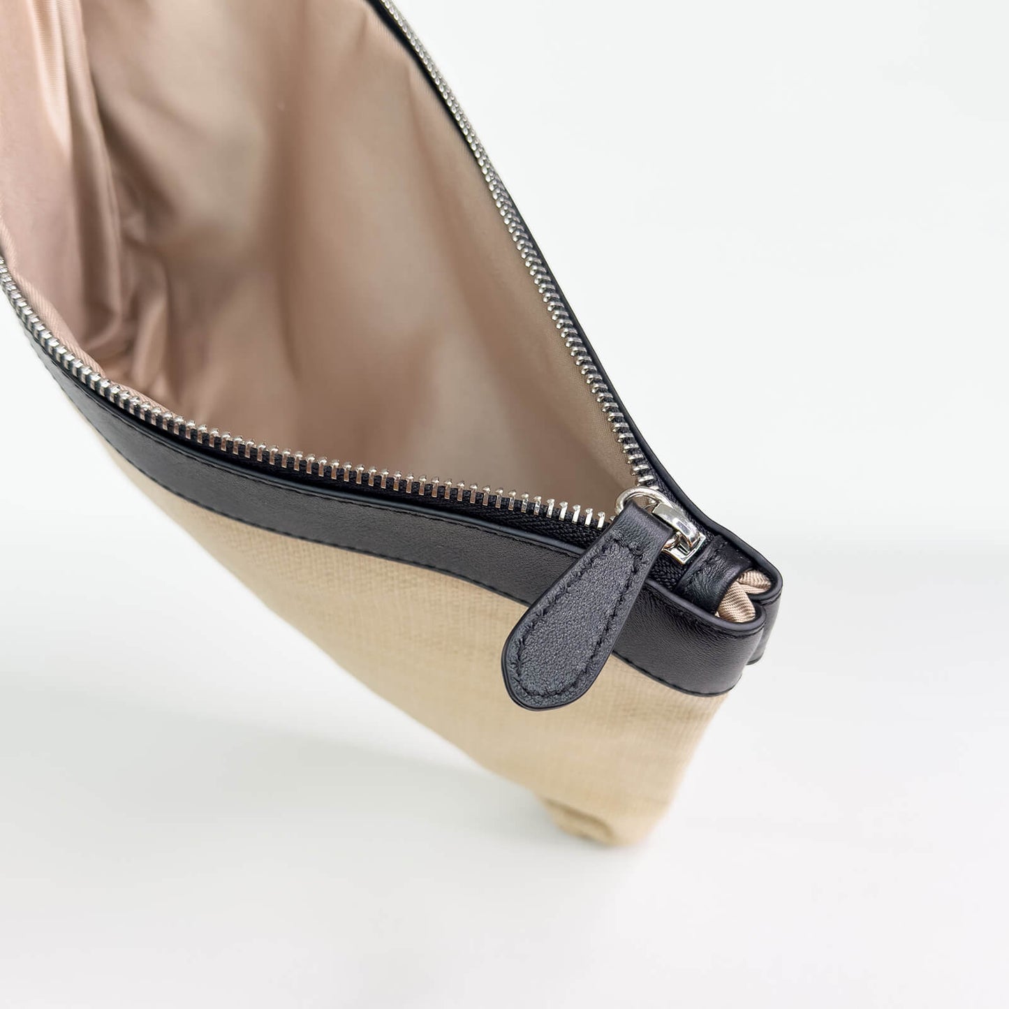 Beige pouch with black leather trim and black zipper on a white background