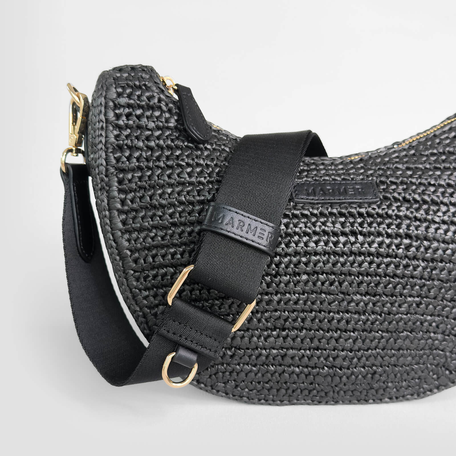 Black woven crocheted handbag with a strap on a light gray background