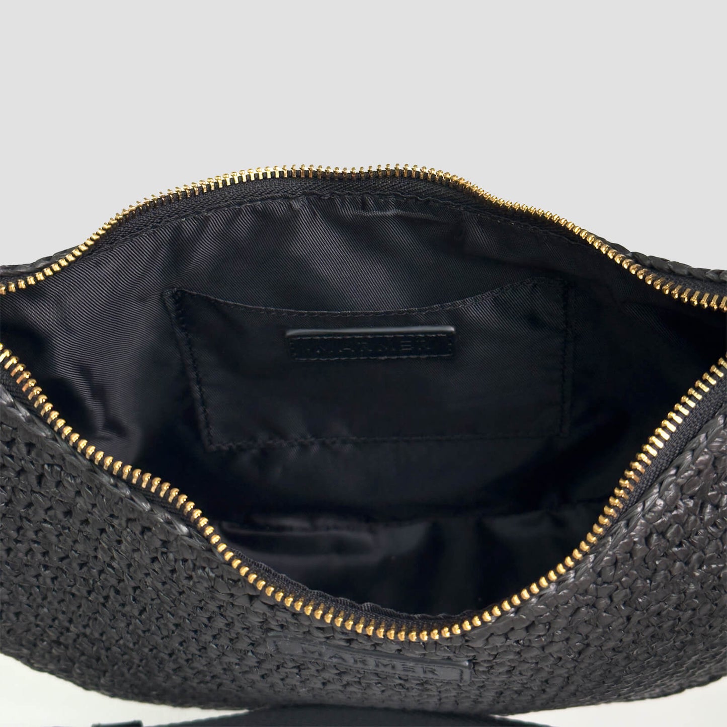 Black woven crocheted bag with gold zipper on a light gray background