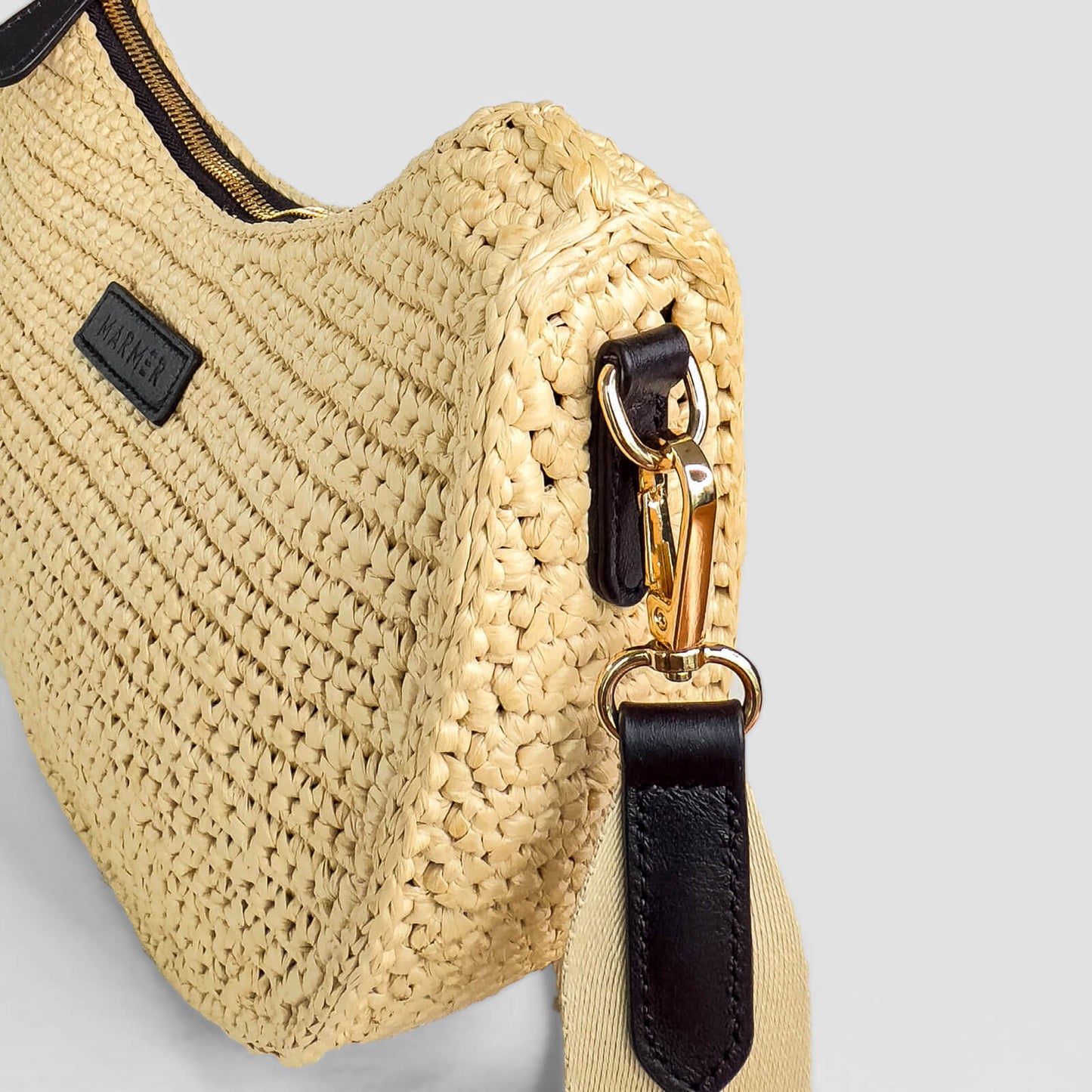 Beige woven handbag with black strap and gold zipper on a light gray background