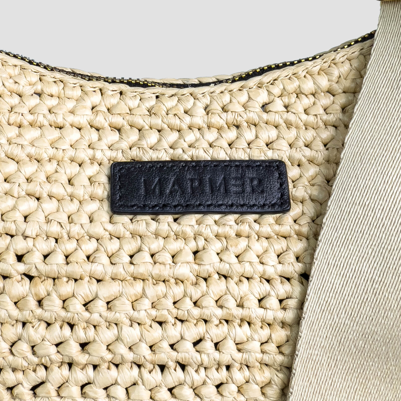 Close-up of a woven beige bag with a black label on a light gray background