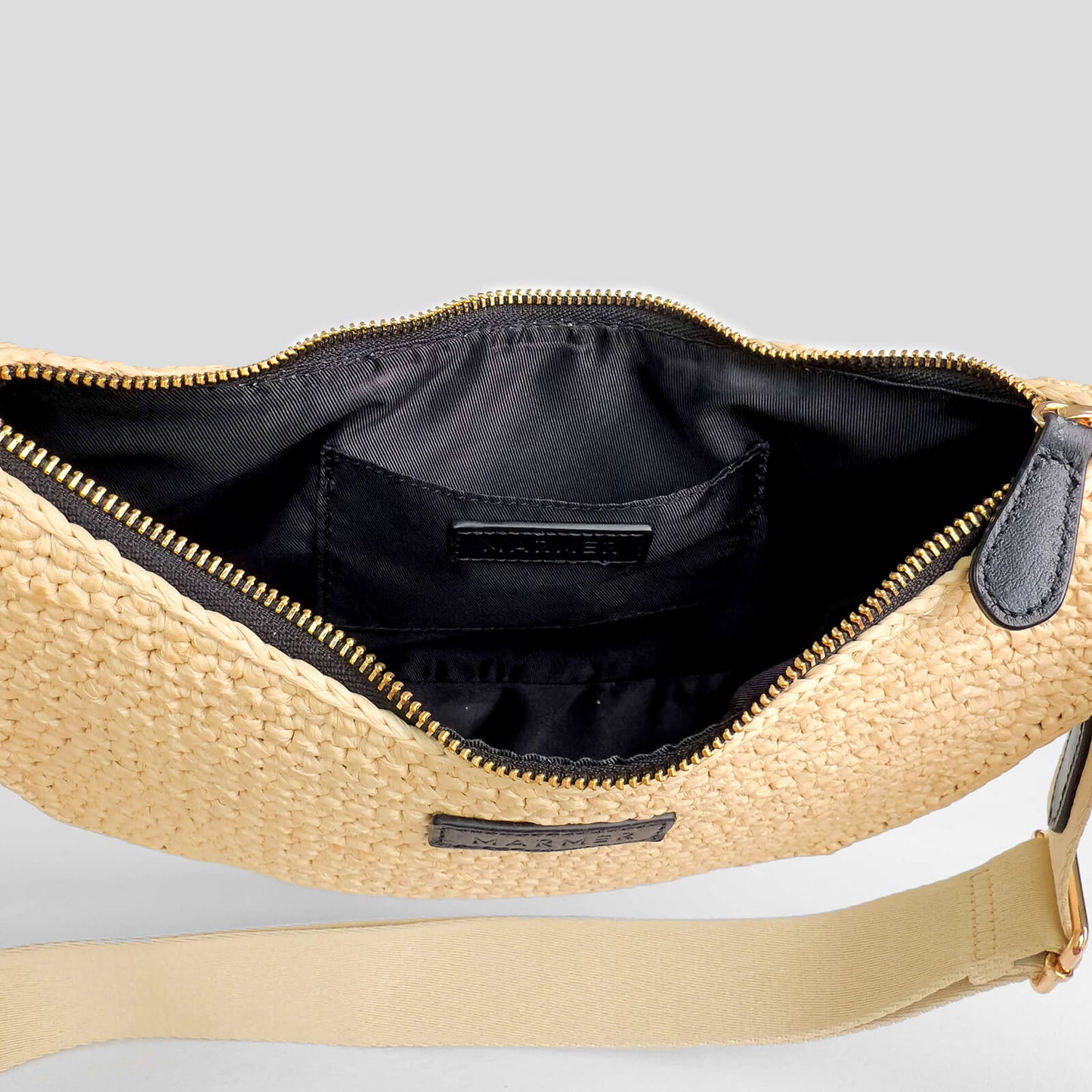 Beige straw bag with gold zipper and strap on a light gray background