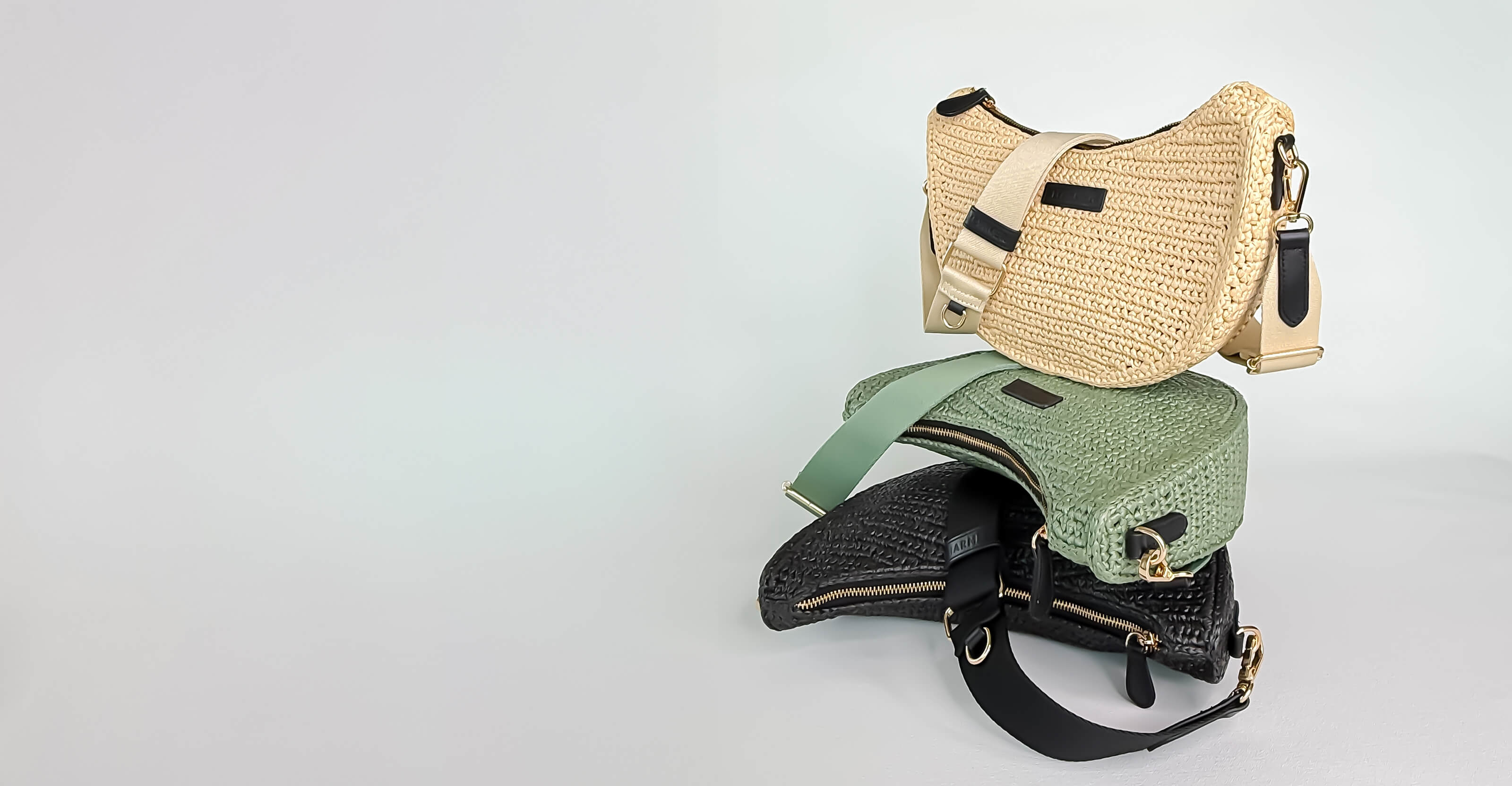 Collection of handbags including a straw bag, green textured bag, and black leather bag on a light gray background