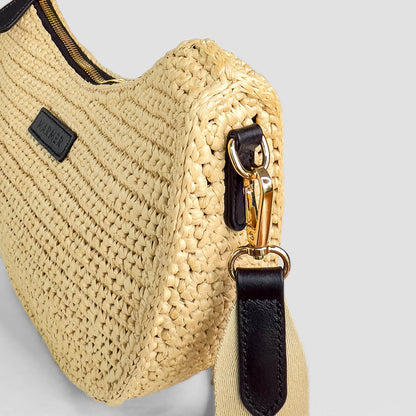 Beige woven handbag with black strap and gold zipper on a light gray background